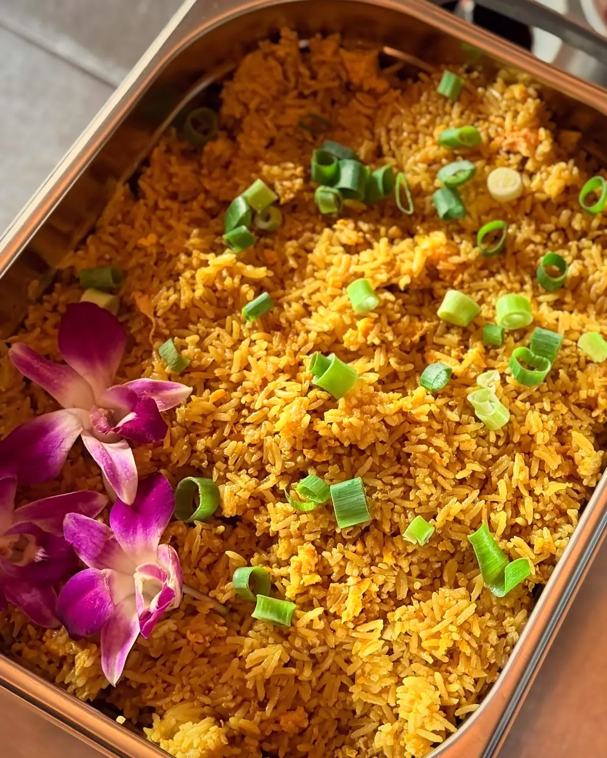 Gele gebakken rijst met lente-ui en orchideeën in een buffetschaal