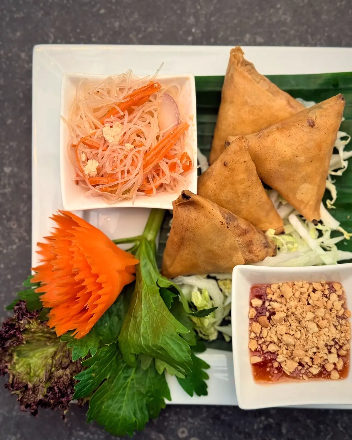 Samosa’s, glasnoedelsalade en sausjes op een bananenblad